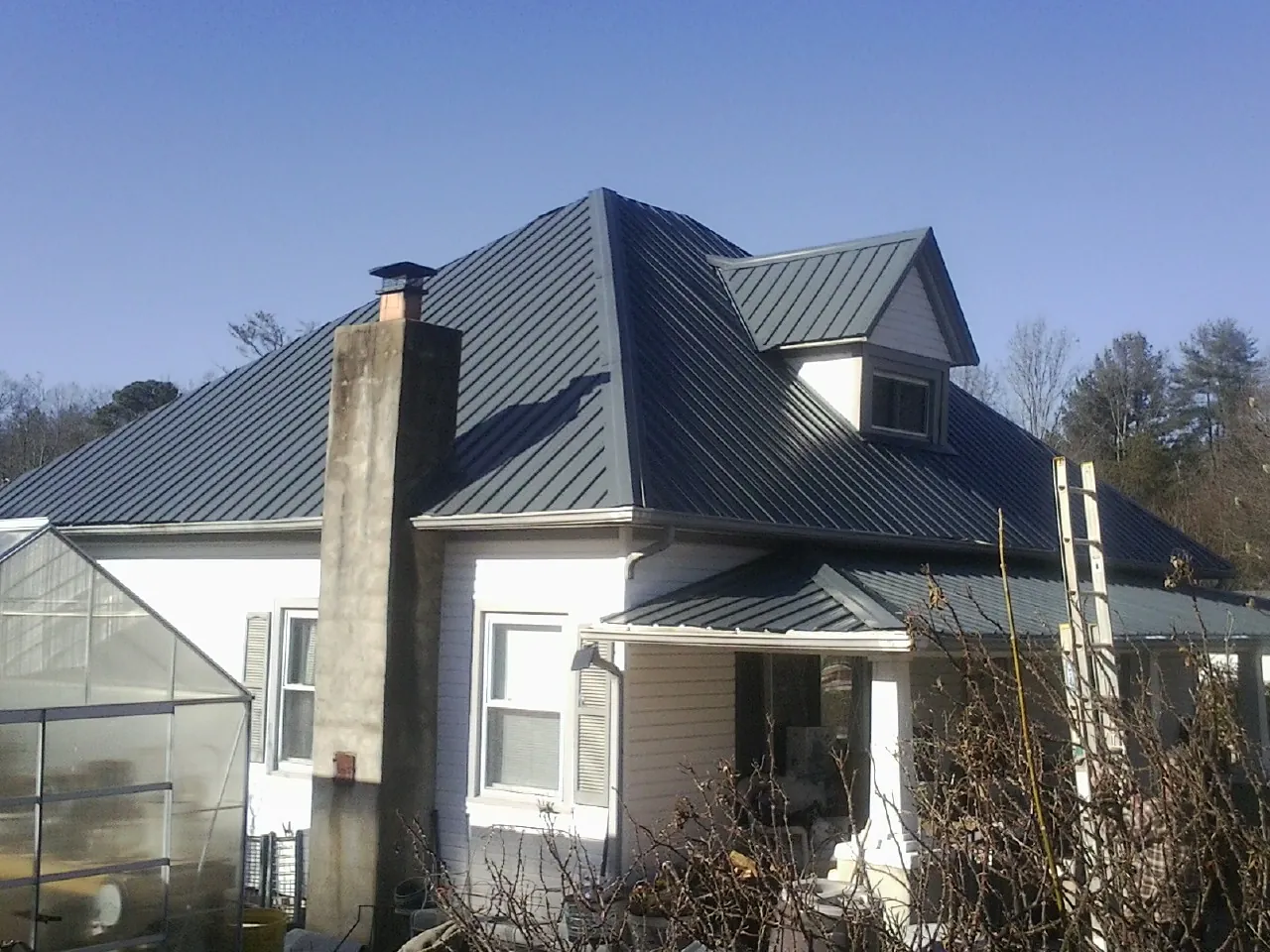 Dark blue standing seam metal roof on a white farmhouse with dormer — Slate & Tile Roof Repair by Roofing Brothers in Schuylerville