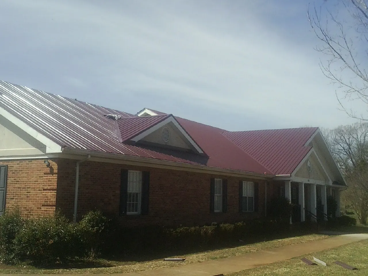 Red metal roof with gabled entries on a long brick building, from a Hail Damage Roof Repair job in Schuylerville