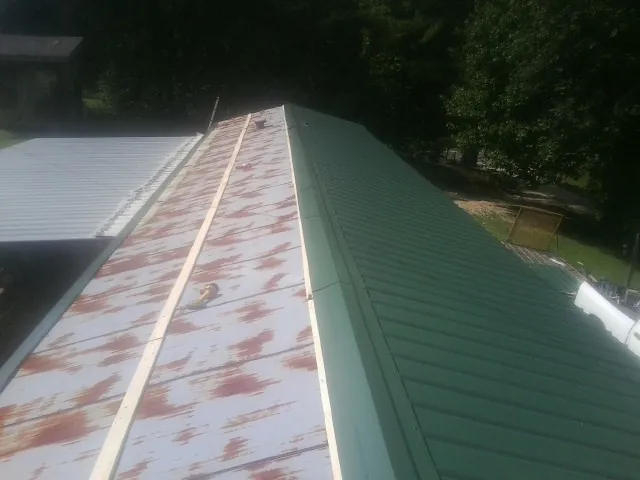 Old rusted panels beside newly installed green metal roofing — Wind Damage Roof Repair by Roofing Brothers in Schuylerville