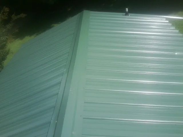 New green metal panels meeting at the ridge of a roof — Flat Roof Repair work by our crew in Schuylerville
