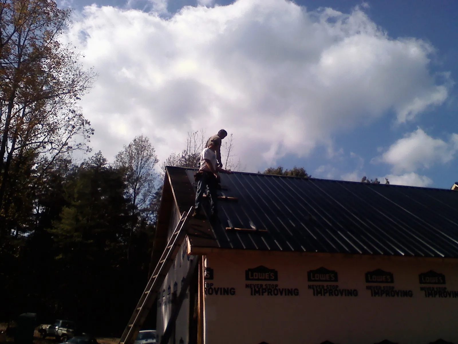 Roofer fastening dark metal panels high against a cloudy sky, from a Roof Inspection job in Schuylerville