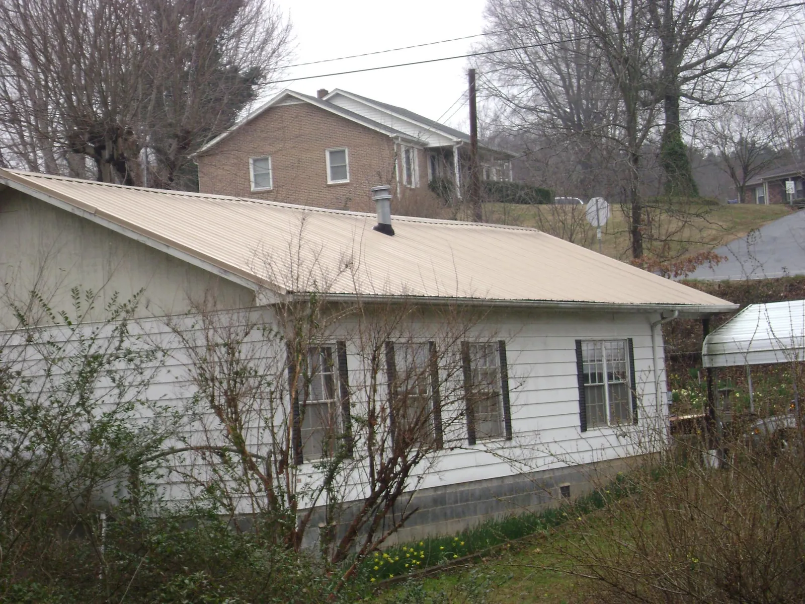 Tan metal roof on a white sided house set into a hillside — Commercial Roofing by Roofing Brothers in Schuylerville